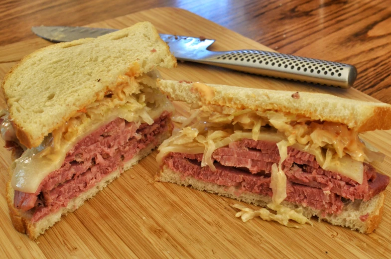 corned beef sandwich sliced in half on  board with knife