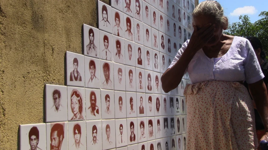 an elderly woman leaning against a wall in front of multiple images on it