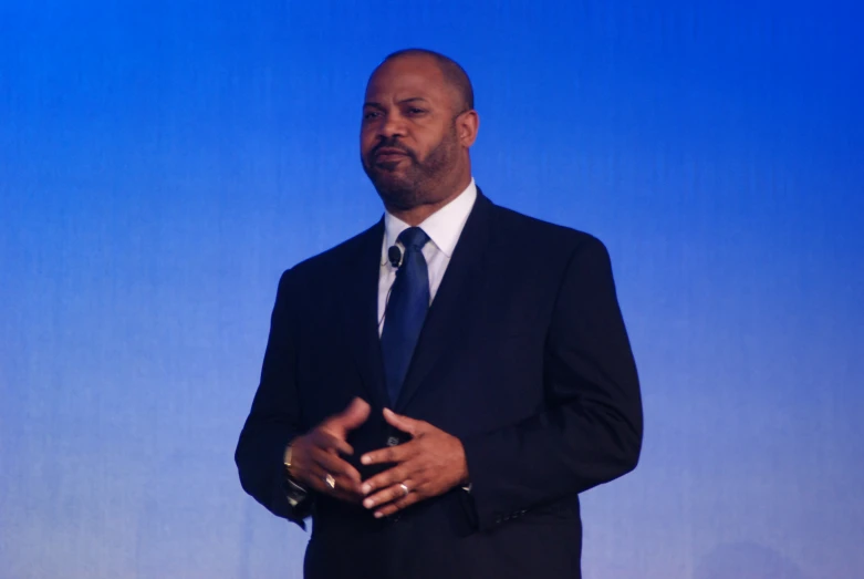 man in black suit with hand on chest standing