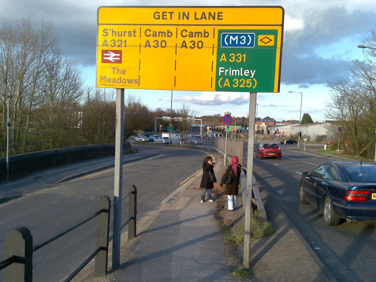 a highway sign reads get in lane and two women are walking