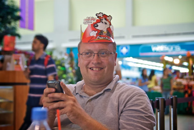 a man wearing a red paper hat is texting on his phone