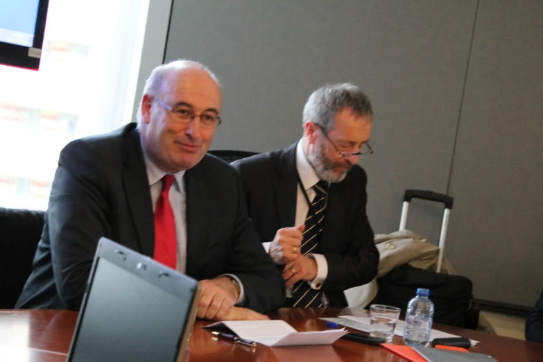 a man in a suit and tie sitting in front of two laptops