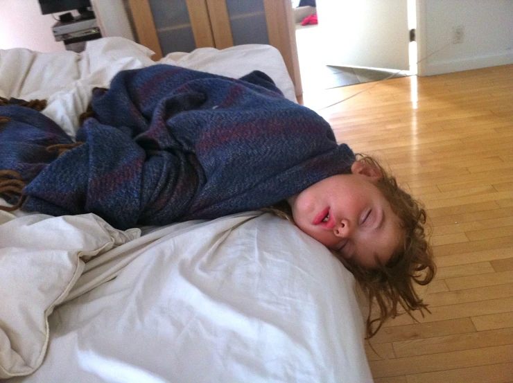 a boy laying on top of a bed on a wooden floor