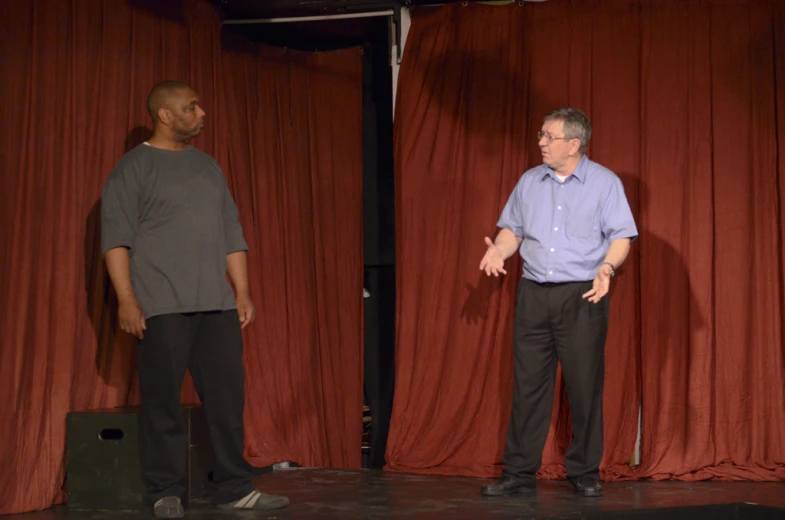 two men are standing by a red curtain