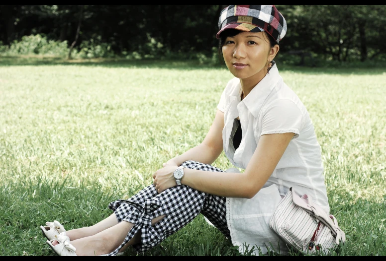 young woman sitting on the grass in front of some trees