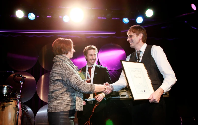 a man and woman standing next to each other while handing him an award