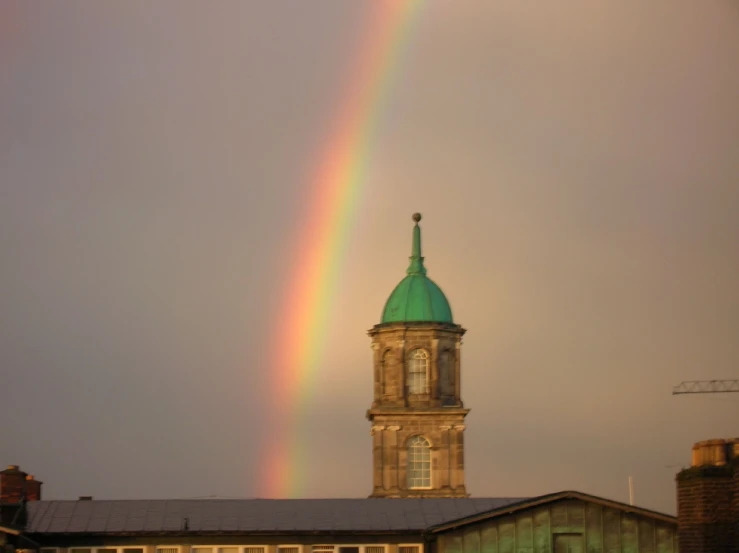 a clock tower with a green top and a rainbow in the sky