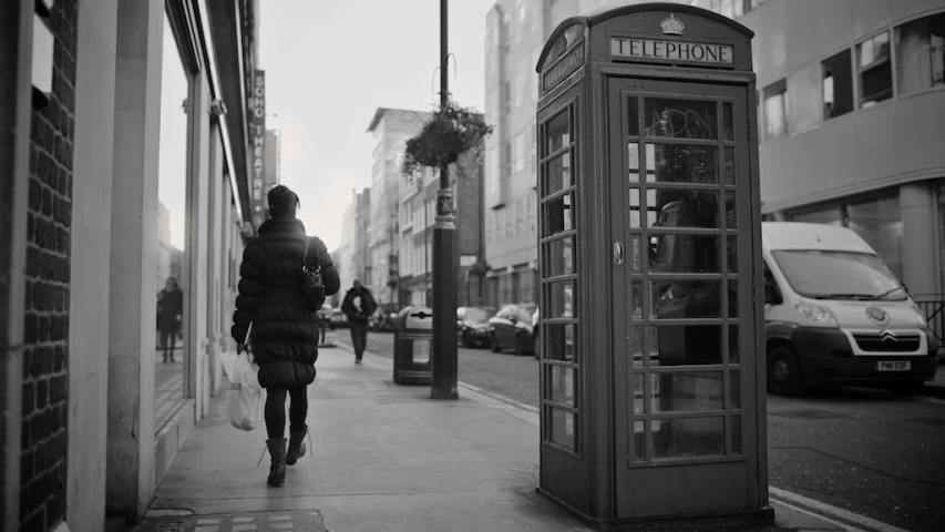 a person on a sidewalk near a telephone booth