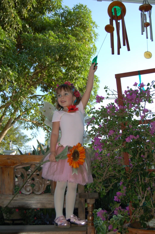 a little girl holding up an orange flower while standing on a bench