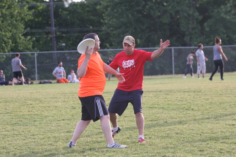 a man throws his hand toward another while people play frisbee in the background