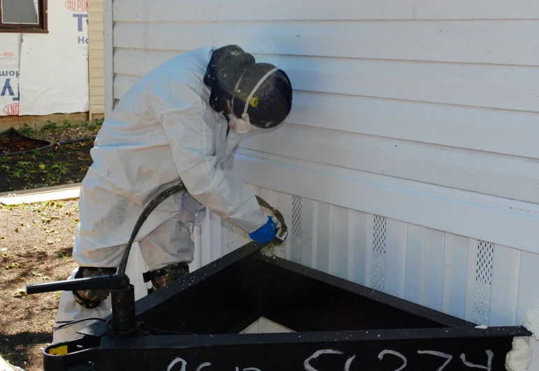 a worker in a white outfit is painting the outside wall