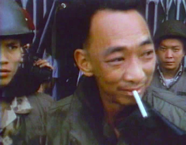 a man smoking a cigarette with two people in the background