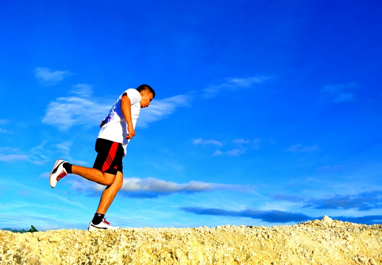 man running up and down sand dune with blue sky in the background