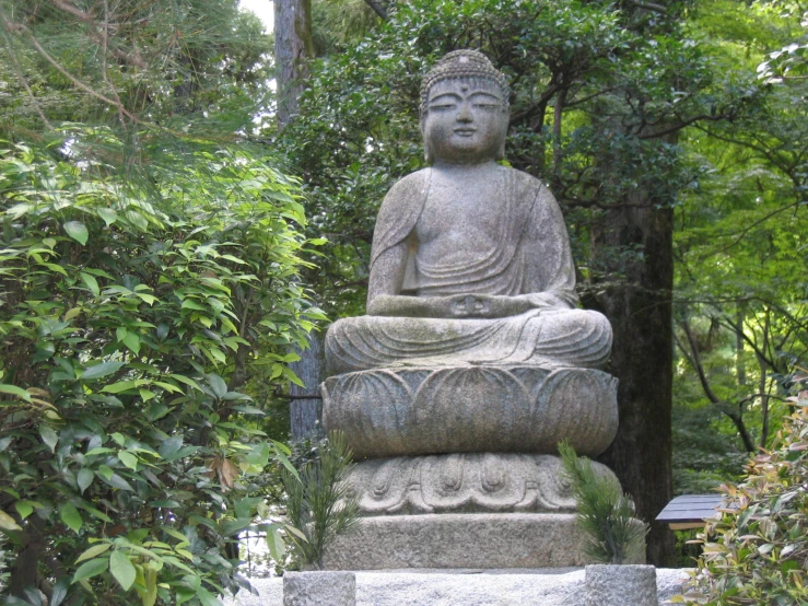 a large grey buddha statue sitting under trees