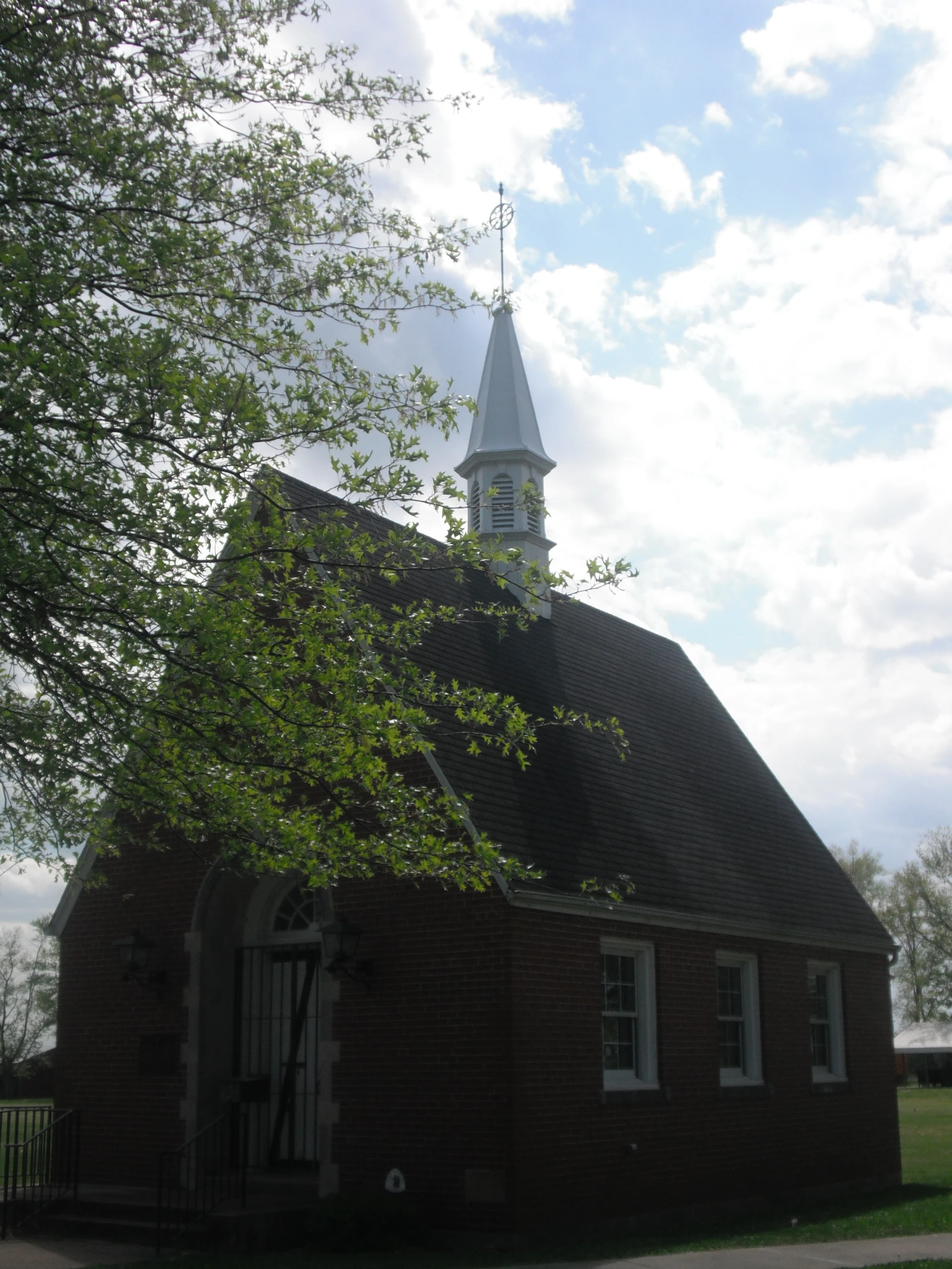 a small brick church with a steeple and trees in the background