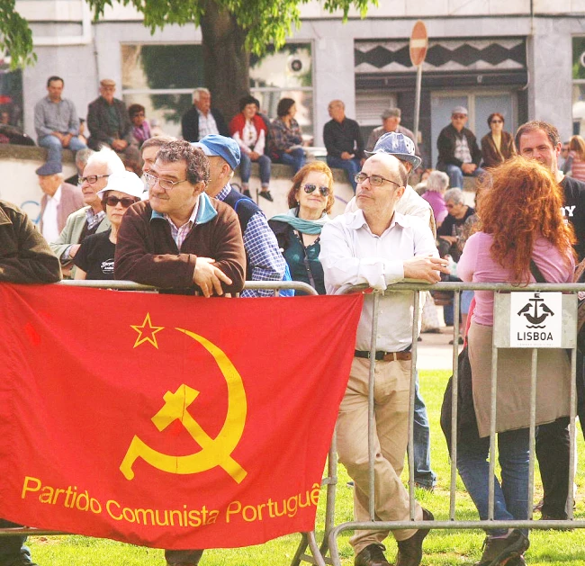 a crowd of people watching a demonstration with a communist flag