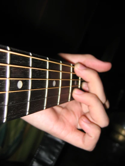 someone holding the neck of a black guitar with a thin fret