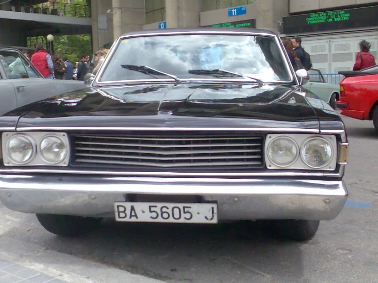 the front end of a black older car on a city street