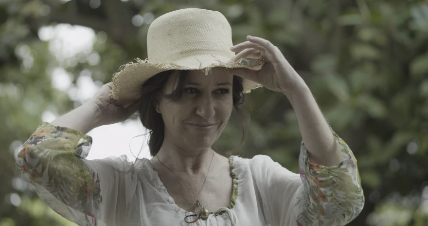 a woman stands smiling and wearing a straw hat