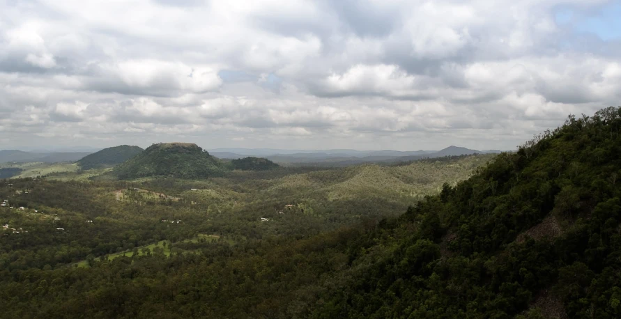 a mountain with some trees on top and some clouds in the sky