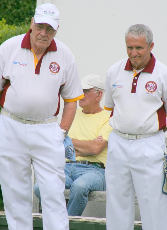 three older men in white pants and red and yellow tops are standing next to each other