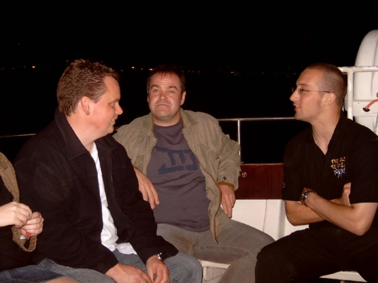 three men sitting on a bench at night
