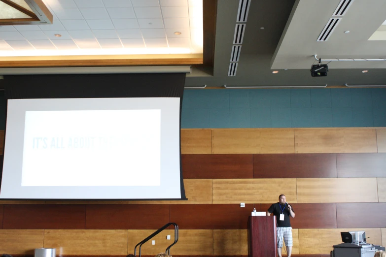 a man in a suit at a podium standing in front of a projector screen