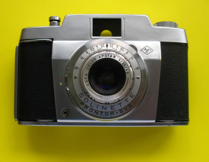 a compact camera laying on a yellow background