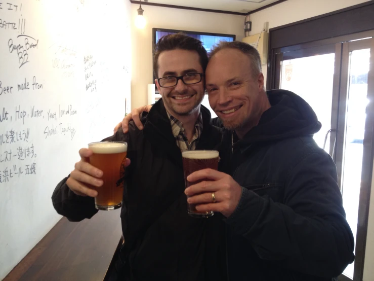 a pair of men smile as they are holding beer