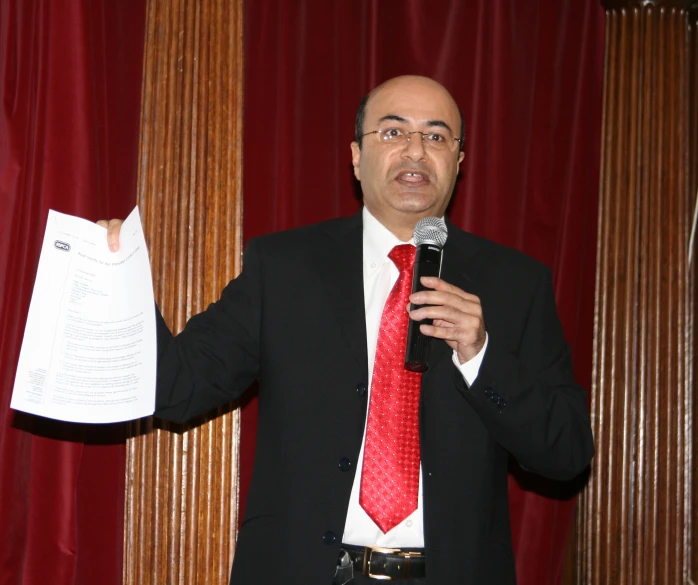 a man giving a speech in front of two red curtains