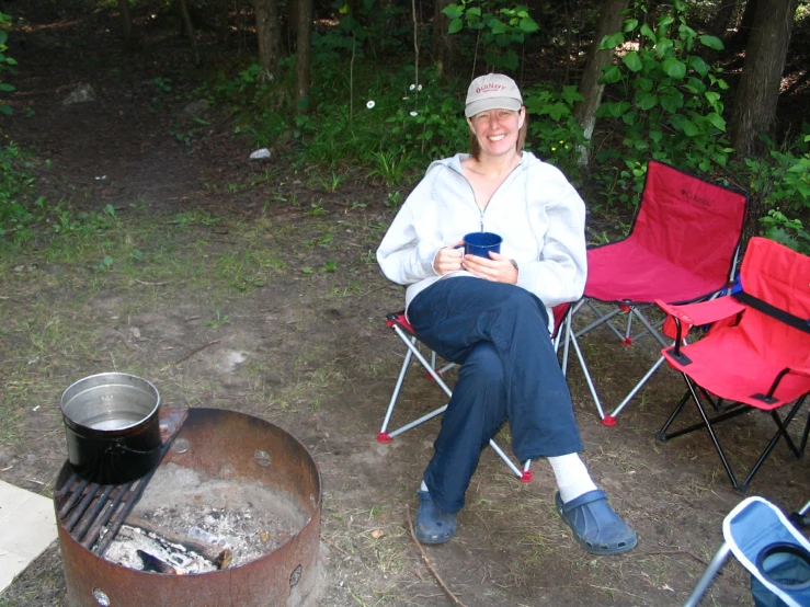 the woman sits by the campfire and drinks coffee