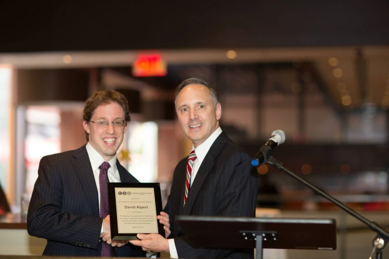 two men dressed in business suits stand next to a microphone