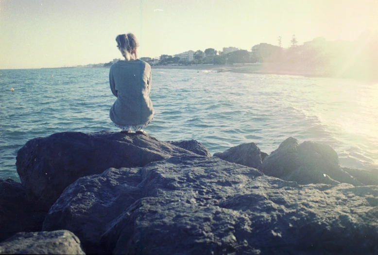 there is a girl that is sitting on a rock looking out at the water