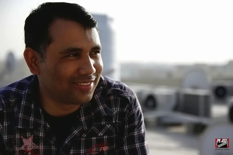 a man with a plaid shirt and beard sitting outside