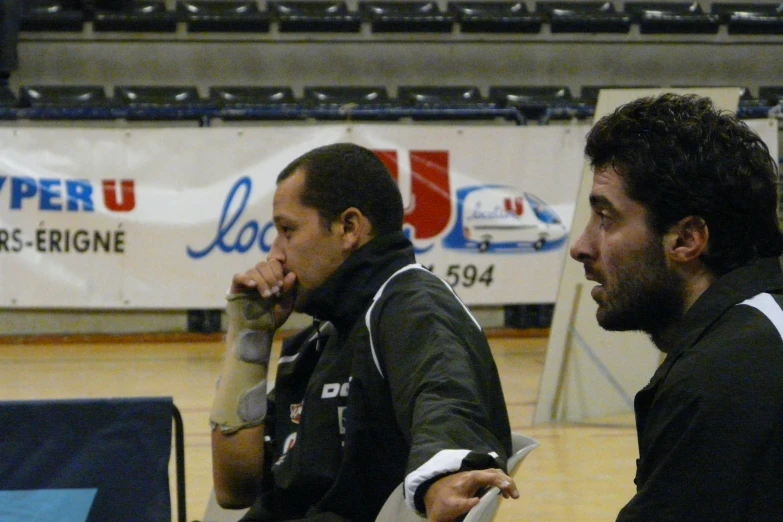 two men sit together on the floor of a gymnasium