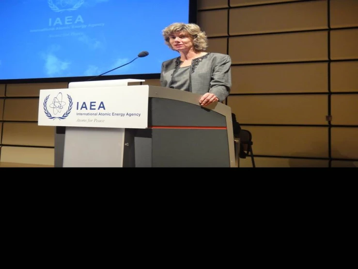 a woman standing in front of a podium with a projection screen behind her