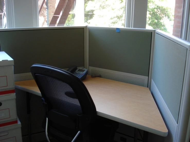 an office cubicle with a chair, phone and some folders