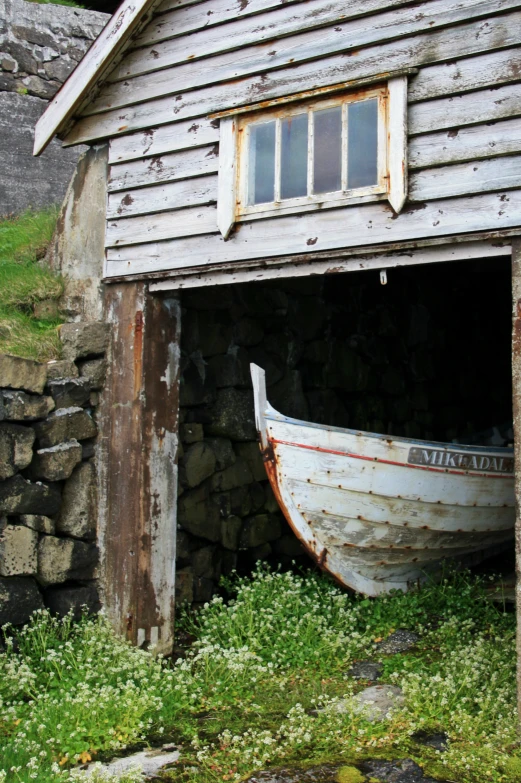 an old boat sitting in the grass under a building