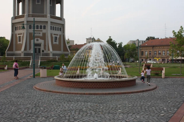 children are walking around a fountain with water shooting