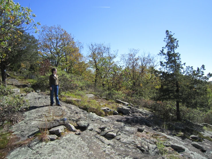 a woman in black shirt standing on rock covered hillside