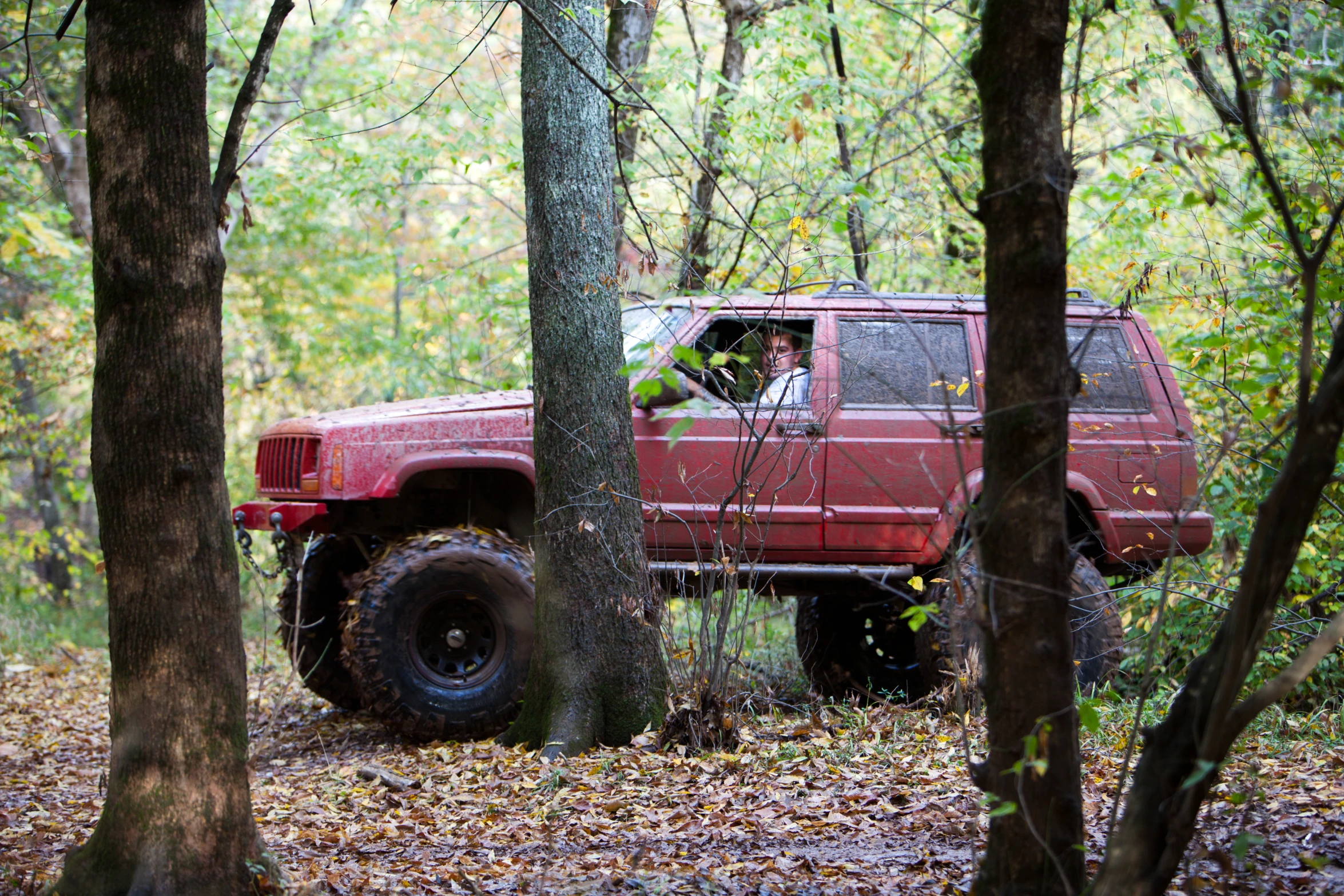 a red truck with large wheels sitting behind some trees