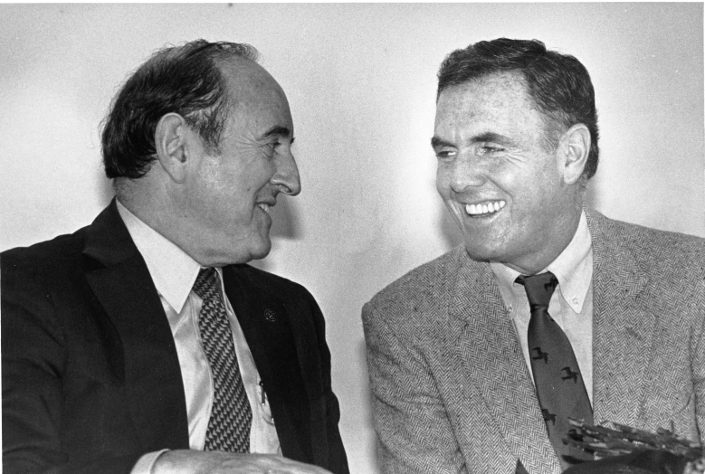 two men in suits smiling at each other