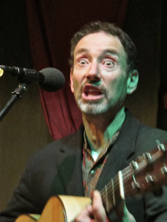 man playing guitar in front of microphone on stage