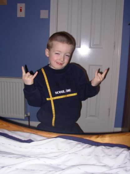 a small boy sitting on top of a bed making the peace sign