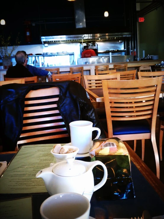 a coffee house with empty tables, empty chairs, a wooden table, and several cups