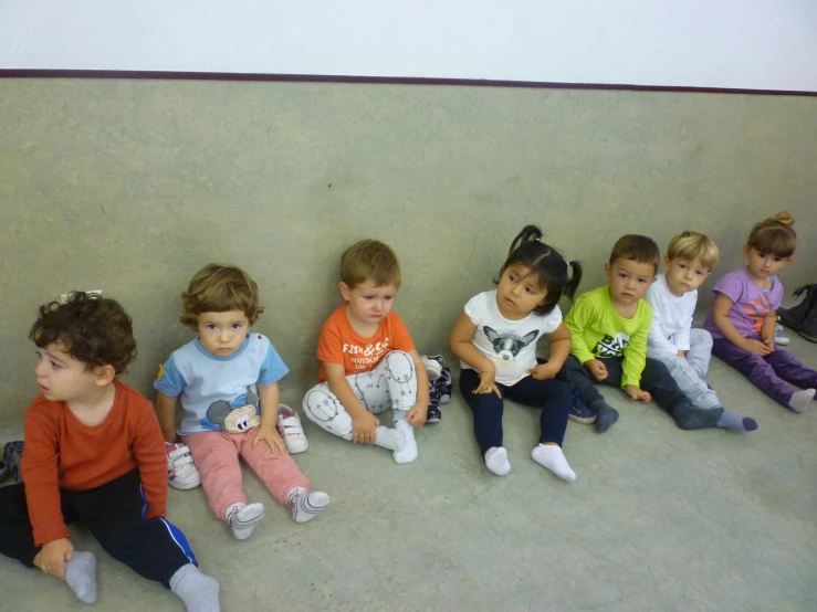children sitting on the floor in front of a wall with small stuffed animals