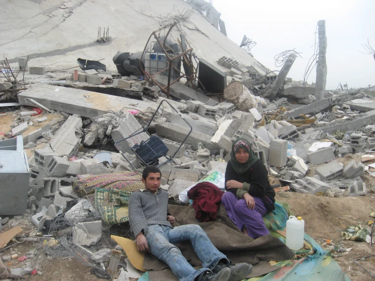 two men sitting on the ground among rubble and debris