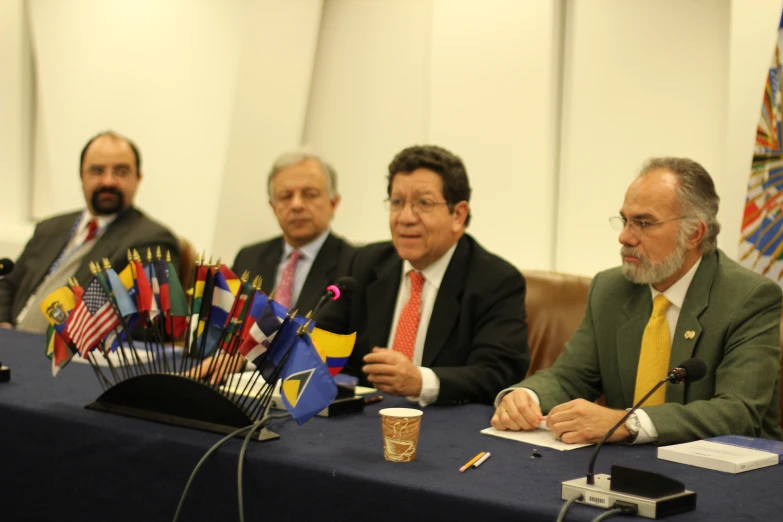 several men sitting in front of a table with flags