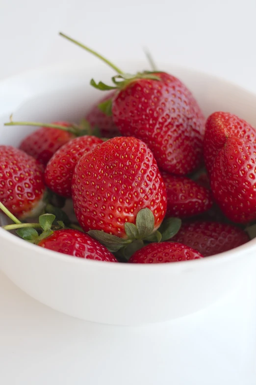 a bowl filled with strawberries, on a white surface