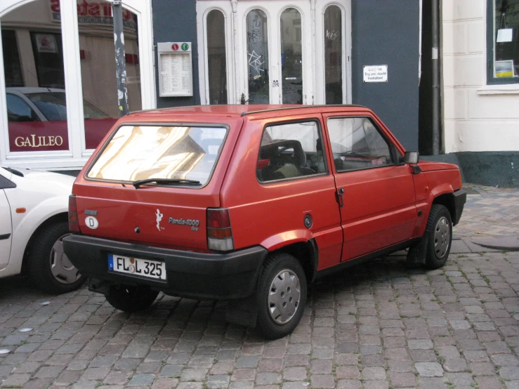 a small red car parked on the street in front of a building